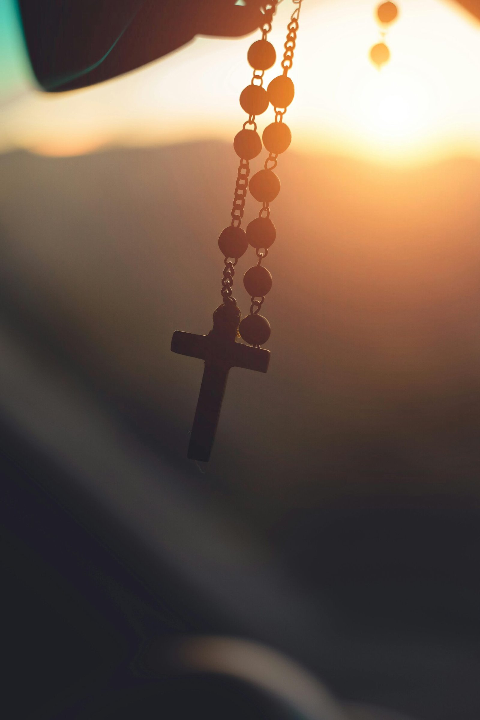 Accueil Silhouette of a rosary cross hanging with sunrise background in Brazil, capturing spiritual serenity.